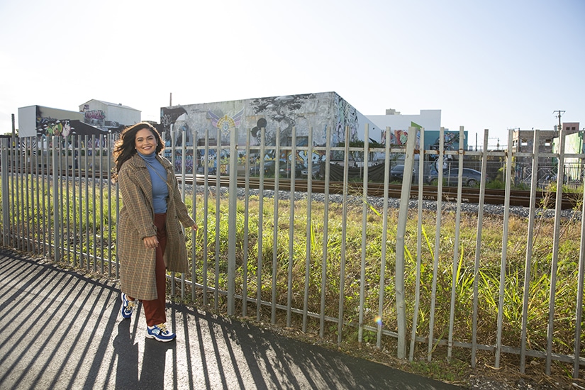 Karli Henriquez walking down a sidewalk along a fence in Miami