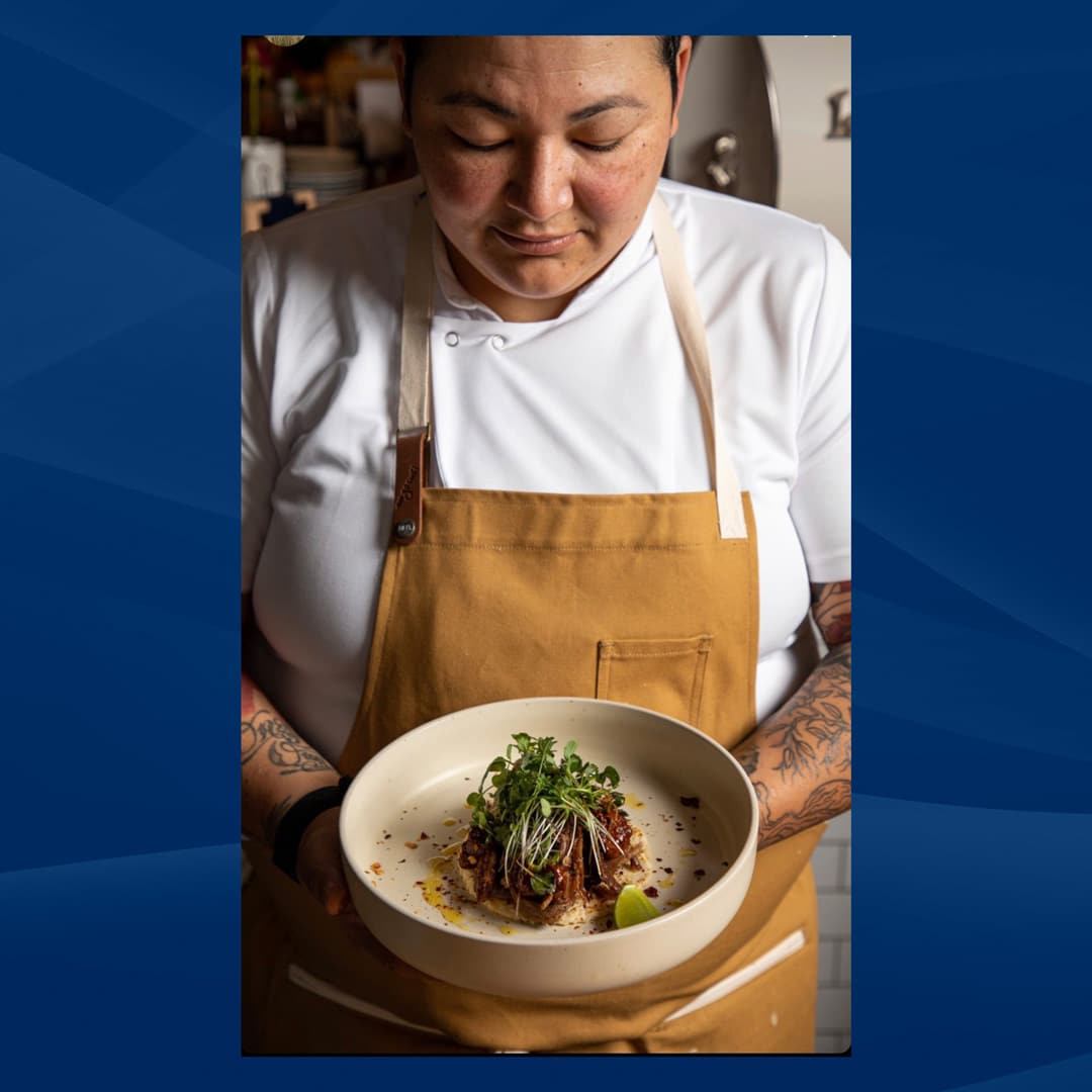 Headshot of Chef Melissa Araujo where she wears an old gold apron and looks down at a bowl of one of her culinary creations.