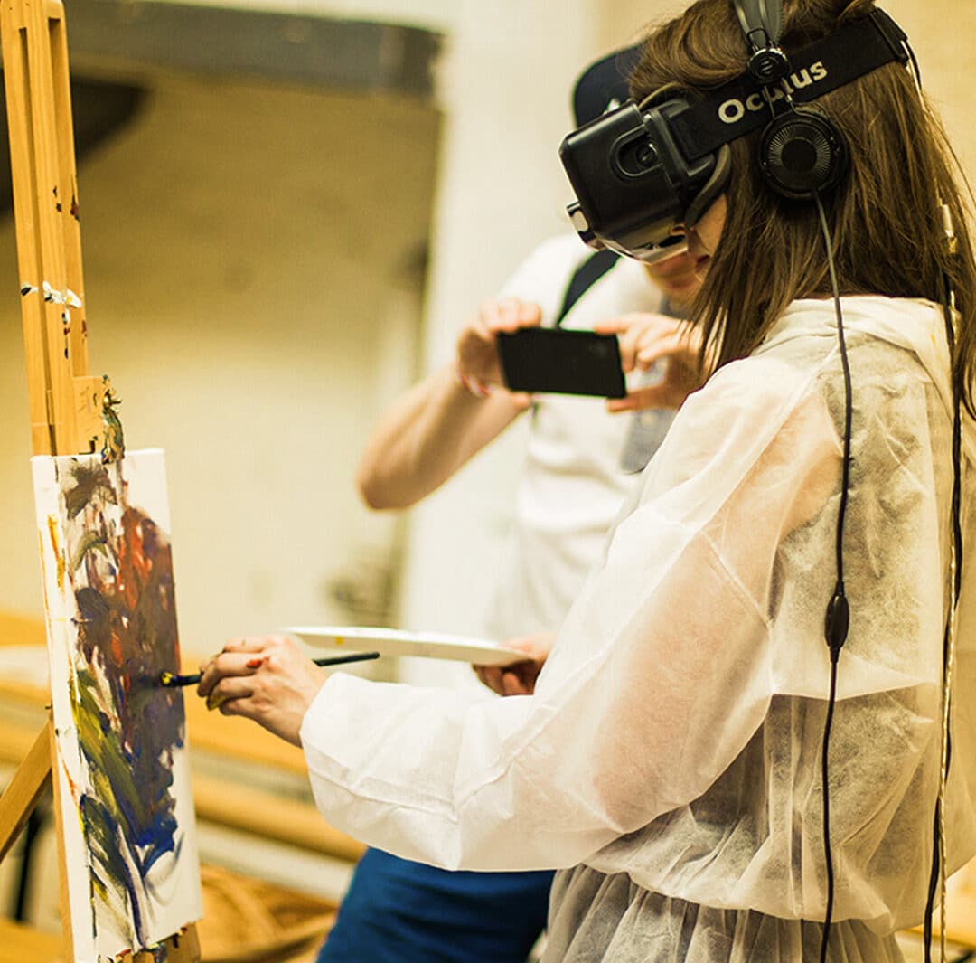 A woman wears a VR Oculus headset while painting on a canvas