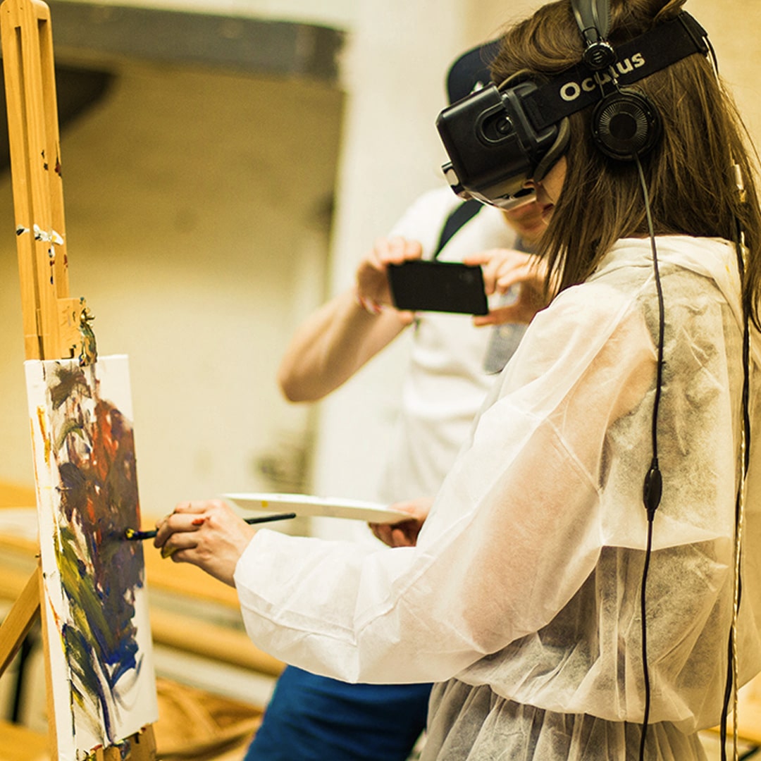 A woman wears a VR Oculus headset while painting on a canvas