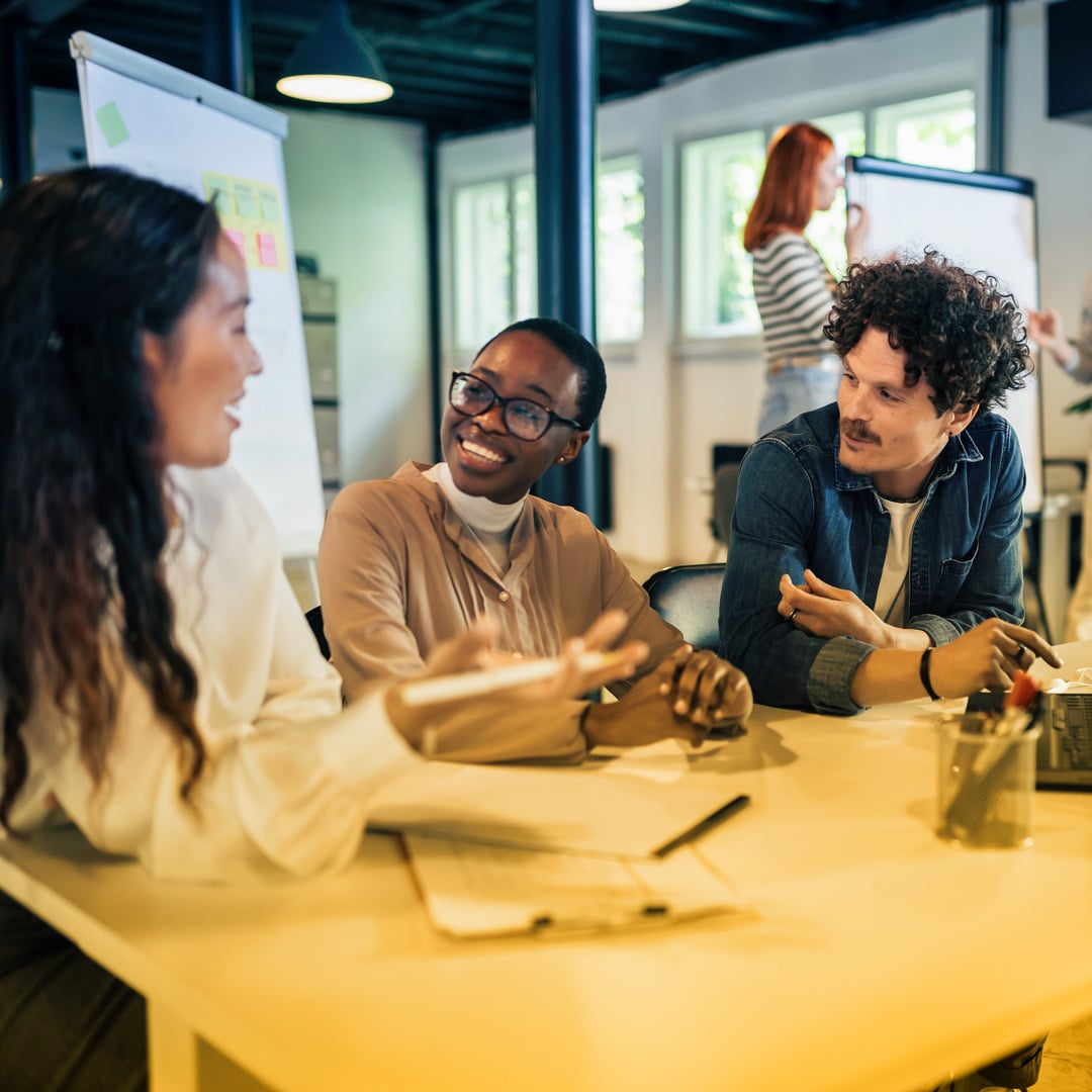 Two women of color and a man sit at a table in conversation with each other with documents laid in front of them