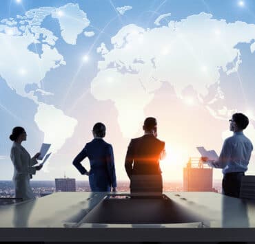 Two men and two women stand facing away from the viewer, looking out over a city with the global map transparent above them in the background