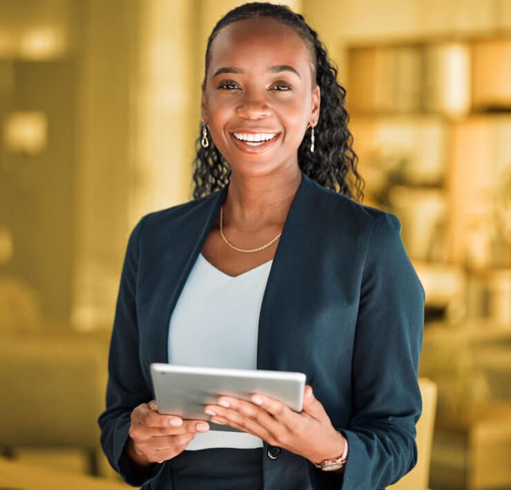 A headshot of a woman of color holding a tablet and smiling at the camera with a yellow background