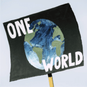 A picketing poster picturing the globe against a black background with the words "ONE WORLD" in white