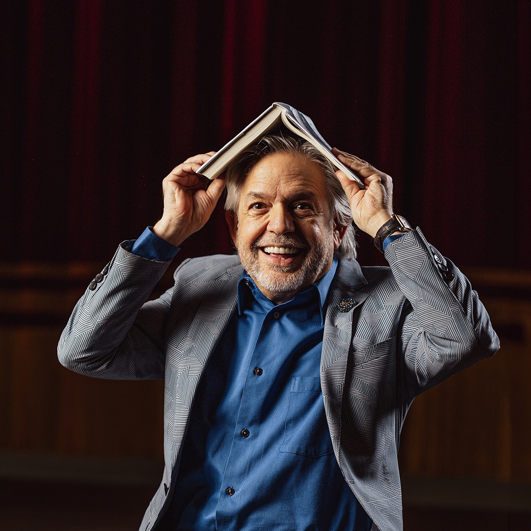 A grinning Luis A. Miranda Jr. holds an open copy of his memoir Relentless over his head like a hat