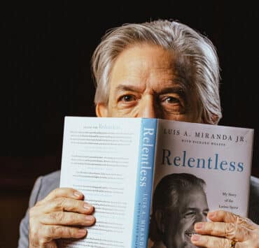 Luis A. Miranda Jr. holds his memoir Relentless open with the cover facing out, and the book is cover all but his eyes and the top of his head